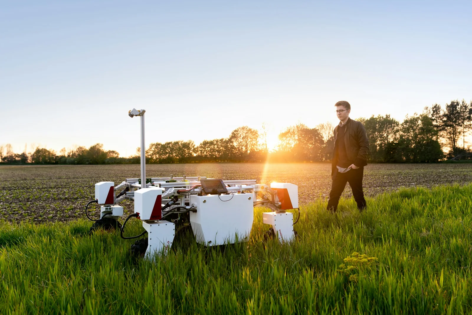 An engineer beside an agricultural robot in a field at sunset